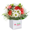 Joy radiates from this uplifting floral arrangement, cradled in a sleek white gift bag, ready to brighten a Guildford doorstep. The bouquet bursts with soft coral and peach carnations, each densely ruffled petal inviting a sense of gentle warmth and affection. Splashes of vibrant red carnations create an energetic contrast, while crisp white daisies with sparkling greenish-yellow centers bring a sense of cheerful innocence-like wildflowers spotted along the outskirts of Pewley Down. Airy clusters of baby's breath lend the bouquet a wistful, cloudlike texture, their presence lightening the look and spirit of the piece. Subtle purple-tinged buds nestle gracefully among the foliage, their quiet hues a nod to the delicate wild blooms found near Guildford's woodlands in early spring. The outer ring of rich, glossy green leaves provides a supportive embrace, both grounding and elevating the composition. The entire bouquet is carefully designed in a graceful, rounded shape, celebrating the art of local floristry and the attention to detail cherished within the community. The white gift bag, with its ribbon handles, is not only a mark of stylish presentation but ensures the flowers arrive fresh and beautiful, whether for a birthday surprise on Onslow Street or an anniversary gesture in Charlotteville. Every bloom and leaf reflects the heartfelt care that defines flower delivery in Guildford-a gift that promises to bring genuine delight and warmth to any thoughtful occasion.
